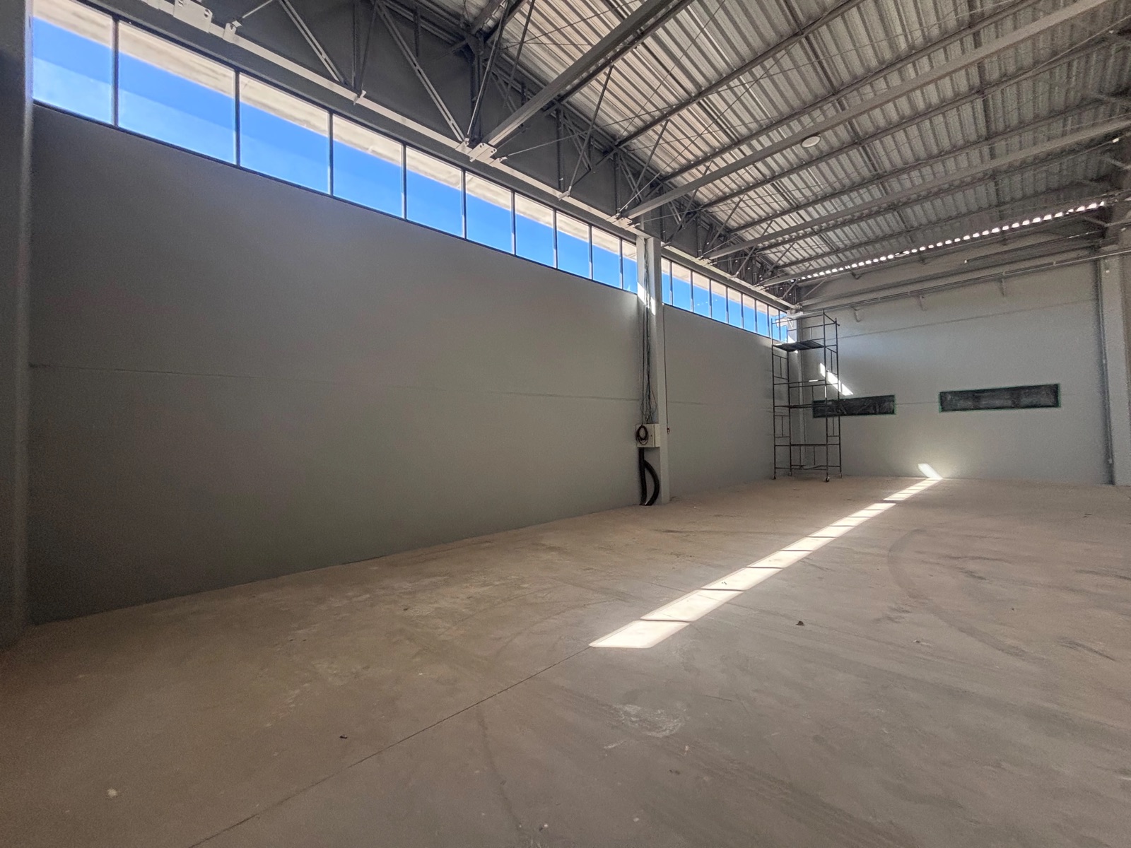 Interior do galpão comercial com parede lateral, janelas altas e estrutura de cobertura